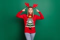 Portrait of attractive amazed funky girl wearing ugly sweater demonstrating horns December tradition isolated over green
