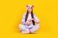 Portrait of attractive amazed girl sitting lotus pose eating corn watching series isolated over bright yellow color