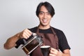 Portrait of attractive Asian barista man in brown apron pouring coffee into a cup from French press coffee maker. Isolated image Royalty Free Stock Photo