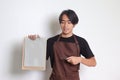 Portrait of attractive Asian barista man in brown apron showing blank paper of menu on clipboard. Isolated image on white Royalty Free Stock Photo
