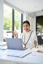 Portrait, Attractive Asian businesswoman sits at her office desk, sipping coffee and waving hand Royalty Free Stock Photo