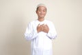 Portrait of attractive Asian muslim man in white shirt with skullcap placing hand on heart, feeling very grateful. Isolated image Royalty Free Stock Photo