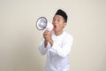 attractive Asian muslim man in white shirt with skullcap speaking louder using megaphone, promoting product.