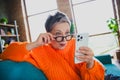 Portrait of attractive astonished lady sit sofa arm touch eyewear use smart phone read news apartment indoors