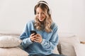 Portrait of attractive blond girl 20s wearing headphones using smartphone and listening to music at home Royalty Free Stock Photo