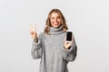 Portrait of attractive blond girl with tattoo, showing smartphone screen and peace sign, stick tongue and smiling happy Royalty Free Stock Photo