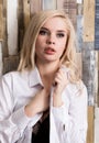 Portrait of attractive blonde girl standing on wood wall background. She has blue eyes and dressed in a man`s shirt Royalty Free Stock Photo