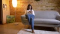 Portrait of attractive brunette businesswoman sitting on sofa and watching with consideration into smartphone at home.