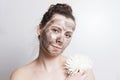 Portrait of attractive brunette girl with black cosmetic face mask and holds white flower. Facial mask skin care. SPA treatments. Royalty Free Stock Photo