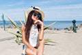 Portrait of attractive brunette girl with long hair sitting on the beach near cactus on the background. She wears hat Royalty Free Stock Photo