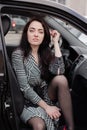 portrait of attractive brunette in grey checkered dress in a black car. girl in automobile. business woman