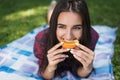 Portrait of attractive brunette woman lying on green grass in outdoor eating orange fruit, copy space for your advertising message Royalty Free Stock Photo