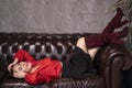 Portrait of attractive brunette woman in red blouse and black skirt lying on leather couch in a vintage cafe. st valentines Royalty Free Stock Photo