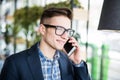Portrait of attractive caucasian man in casual shirt and glasses talking on cellular phone at workplace. Royalty Free Stock Photo
