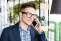 Portrait of attractive caucasian man in casual shirt and glasses talking on cellular phone at workplace. Royalty Free Stock Photo