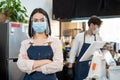 Portrait of attractive Caucasian waitress wearing protective mask to prevent from Covid-19 pandemic at cafe. Young beautiful girl Royalty Free Stock Photo