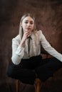 Portrait of caucasian woman wearing white blouse sitting at chair isolated dark background Royalty Free Stock Photo