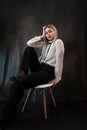 Portrait of caucasian woman wearing white blouse sitting at chair isolated dark background Royalty Free Stock Photo