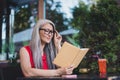 Portrait of attractive cheerful focused grey-haired woman reading oranizer diary sitting at cafe outdoors Royalty Free Stock Photo