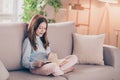 Portrait of attractive cheerful focused preteen girl sitting on divan resting reading book at house flat indoor Royalty Free Stock Photo