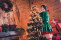 Portrait of attractive cheerful girl elf hanging on tree toys festal day staying at home modern loft industrial interior