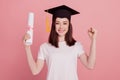 Portrait of attractive cheerful girl graduating holding paper document rejoice victory isolated over pink pastel color