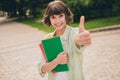 Portrait of attractive cheerful girl holding academic copybook giving thumbup solution deal done on fresh air outdoors