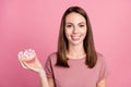 Portrait of attractive cheerful girl holding in hand delicious fresh doughnut isolated over pink pastel color background