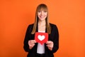 Portrait of attractive cheerful girl holding in hands paper red card like web follow isolated over bright orange color