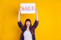 Portrait of attractive cheerful girl holding up presentation sale board ad isolated over bright yellow color background