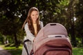 Portrait of attractive cheerful girl walking newborn carriage resting on fresh air spending free time outdoors Royalty Free Stock Photo