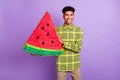 Portrait of attractive cheerful guy holding in hands big watermelon board figure isolated over violet purple color