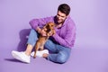 Portrait of attractive cheerful guy sitting spending free time with doggy puppy resting isolated over purple violet