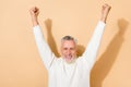 Portrait of attractive cheerful lucky grey-haired man rising hands up having fun isolated over beige pastel color