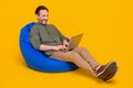 Portrait of attractive cheerful man sitting in chair using laptop programming web isolated over bright yellow color Royalty Free Stock Photo