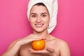 Portrait of attractive cheerful woman with white towel on head, holds orange over pink background. Young smiling female visits spa Royalty Free Stock Photo