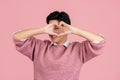 Portrait of attractive cheerful Young asian man wearing pink sweater. He doing heart symbol shape with hands on eyes. romantic Royalty Free Stock Photo