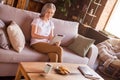 Portrait of attractive cheery focused grey-haired woman using device free time sitting on sofa at home house indoors Royalty Free Stock Photo