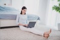 Portrait of attractive cheery focused woman sitting on soft carpet using laptop writing email eshop staying home indoors