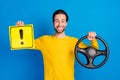 Portrait of attractive cheery guy holding steering wheel sign board isolated over bright blue color background