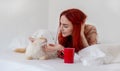 Portrait of an attractive, contented, young, sexy woman, bright red dyed long hair, lying relaxed in morning bed enjoys and Royalty Free Stock Photo
