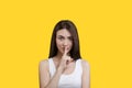 Cute girl holding a finger to her lips in a white top on a yellow background Royalty Free Stock Photo