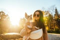 Portrait of an attractive dog-owner female in stylish sunglasses holding her terrier on a sunny day in the park