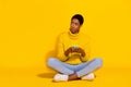 Portrait of attractive doubtful skeptic girl sitting on floor using device copy space isolated on bright yellow color