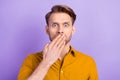 Portrait of attractive embarrassed worried guy closing mouth oops isolated over violet purple color background