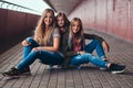 Portrait of an attractive family. Mother and her daughters sitting together on a skateboard at bridge footway. Royalty Free Stock Photo