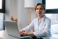 Portrait of attractive female doctor wearing white coat sitting at table with laptop computer and looking camera. Royalty Free Stock Photo