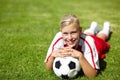 Shes the team captain. Portrait of an attractive female football player lying chest down on the grass and leaning on a