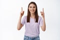 Portrait of attractive female model pointing fingers up, smiling candid, standing in t-shirt, showing advertisement Royalty Free Stock Photo