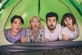 Portrait of attractive four amazed people lying in tent spending free time in park on fresh air having fun outdoors